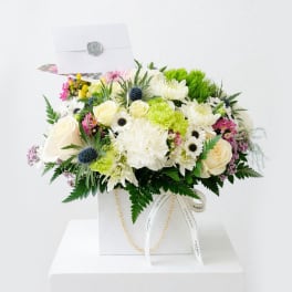 Mixed bouquet of white, cream, pink, and green flowers in a white gift box