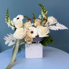 White roses and gerbera daisies arranged in a square ceramic vase