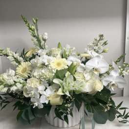 White floral arrangement with orchids, lilies, and pale yellow blooms in a white vase