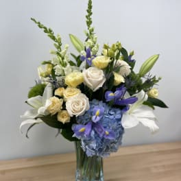 Bouquet of white roses, blue hydrangea, and purple irises in a glass vase