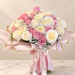 Bouquet of pink and cream roses wrapped in pink paper with ribbon