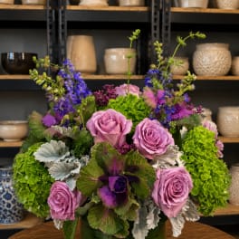 Lavender roses and purple flowers in a green glass vase