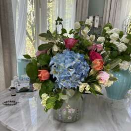 Mixed bouquet with blue hydrangea, pink tulips, and white flowers in a floral tin