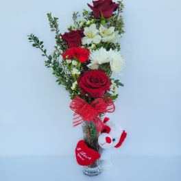Red roses and white flowers in a clear vase with a plush teddy bear