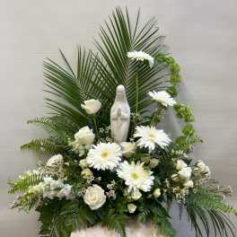 White floral arrangement with a small statue of the Virgin Mary