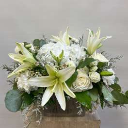 White lilies and roses arranged in a wooden box with greenery