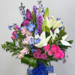 Bouquet of pink roses, white lilies, and blue flowers in a vase with a blue ribbon