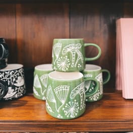 Stacked green ceramic mugs with white botanical patterns on a wooden shelf