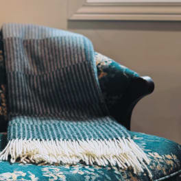 A striped woven blanket draped over a teal floral armchair