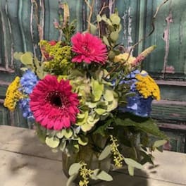 Bright mixed bouquet with pink gerbera daisies and blue and yellow blooms in a vase