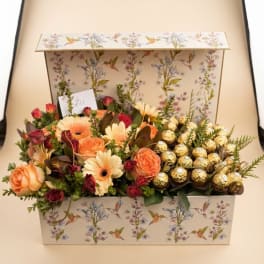 Flower gift box with peach roses, cream daisies, and gold-wrapped chocolates