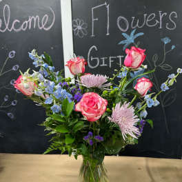 Mixed pink and blue flowers arranged in a clear glass vase