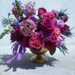Pink and purple flower arrangement in a gold pedestal vase