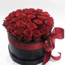 Red roses arranged in a black round box with a red ribbon