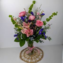 Pink and blue mixed bouquet in a clear glass vase with a pink ribbon