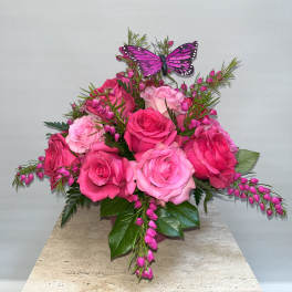 Pink roses with a purple butterfly accent in a vase arrangement