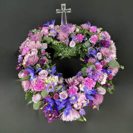 Circular wreath of purple and pink flowers with a clear cross topper