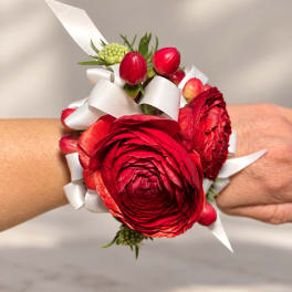 Red flower wrist corsage with white ribbon on a person's wrist