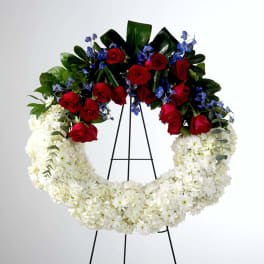 Large floral wreath with red roses, white flowers, and blue accents on a stand