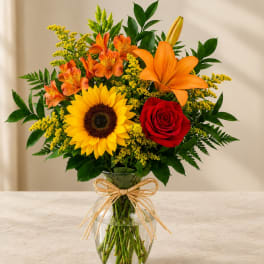Bouquet of sunflowers, roses, lilies, and orange alstroemeria in a glass vase