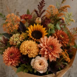 Bouquet of orange, peach, and yellow flowers wrapped in brown paper