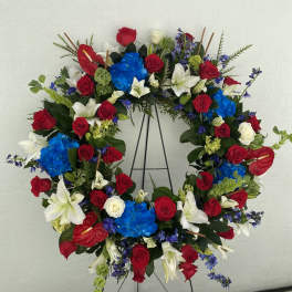 Circular wreath of red roses, white lilies, and blue hydrangeas on a stand