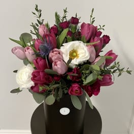 Pink and white tulip bouquet in a black hatbox with greenery