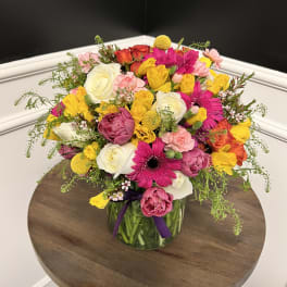 Mixed bouquet of pink, yellow, white, and orange flowers in a glass vase
