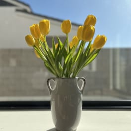 Yellow tulips in a white ceramic vase on a windowsill