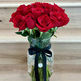 Red roses arranged in a clear glass vase with a dark ribbon