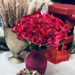 Red rose bouquet in a purple vase with chocolate-covered strawberries in front