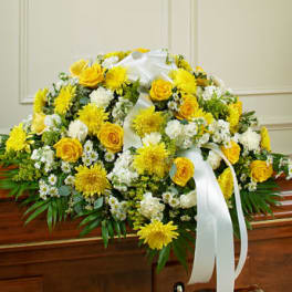 Yellow and white casket spray with roses, mums, and daisies topped with a white ribbon bow.