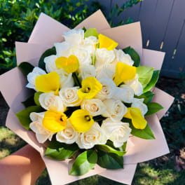 Bouquet of white roses and yellow calla lilies wrapped in pale pink paper