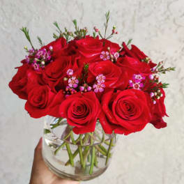 Red roses arranged in a clear glass vase with small pink accent flowers
