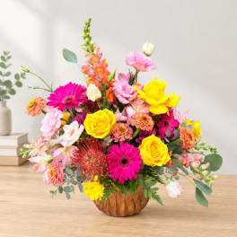 Bright mixed flower arrangement in a brown vase with pink, yellow, and orange blooms.