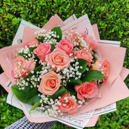 Hand-tied bouquet of peach roses and white filler flowers wrapped in pink paper