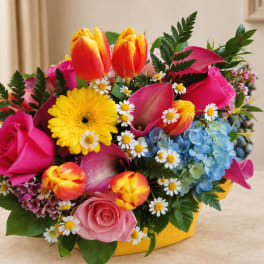 Mixed bouquet with pink roses, tulips, daisies, and blue hydrangeas in a yellow container