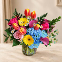 Mixed bouquet of tulips, roses, daisies, and hydrangeas in a glass vase
