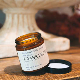 Amber jar of magnesium body butter with a black lid on a wooden surface