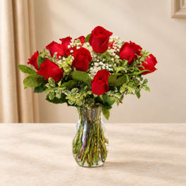 Red roses arranged in a clear glass vase with white filler flowers