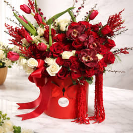 Red and white rose arrangement with tulips in a red hatbox