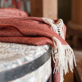 Folded red patterned throw blanket with white fringe draped over a surface