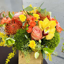 Bright mixed bouquet in a wooden box with yellow, orange, and pink blooms