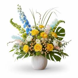 Yellow and white floral arrangement in a white vase with blue accents