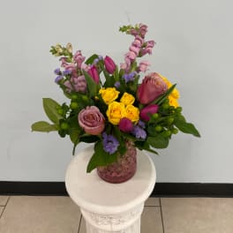 Mixed bouquet of pink, yellow, and purple flowers in a pink glass vase