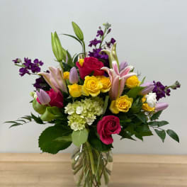 Mixed bouquet of roses, lilies, and purple flowers in a glass vase