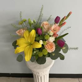 Mixed bouquet of yellow lilies, pink roses, and purple tulips in a white vase