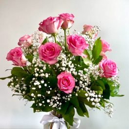 Pink roses in a clear glass vase with white baby's breath and a white ribbon
