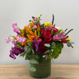 Mixed bouquet in a green glass vase with roses, lilies, and orchids