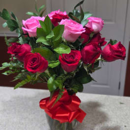 Bouquet of pink and red roses in a clear vase with a red ribbon